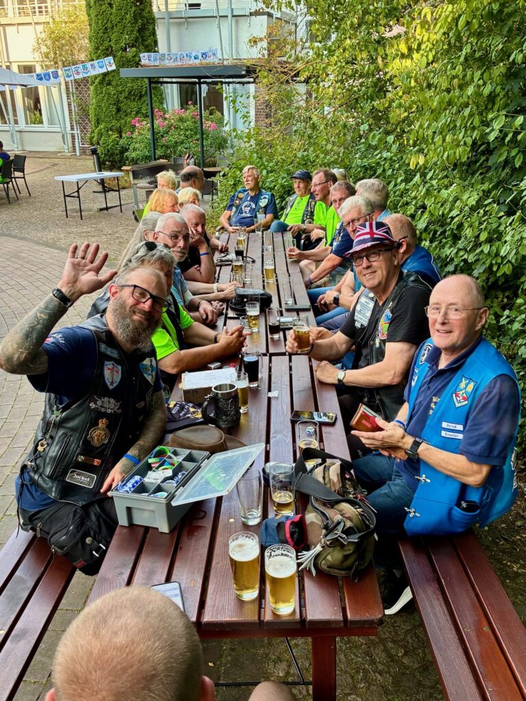 Gäste an einer langen Biertischreihe winken in die Kamera