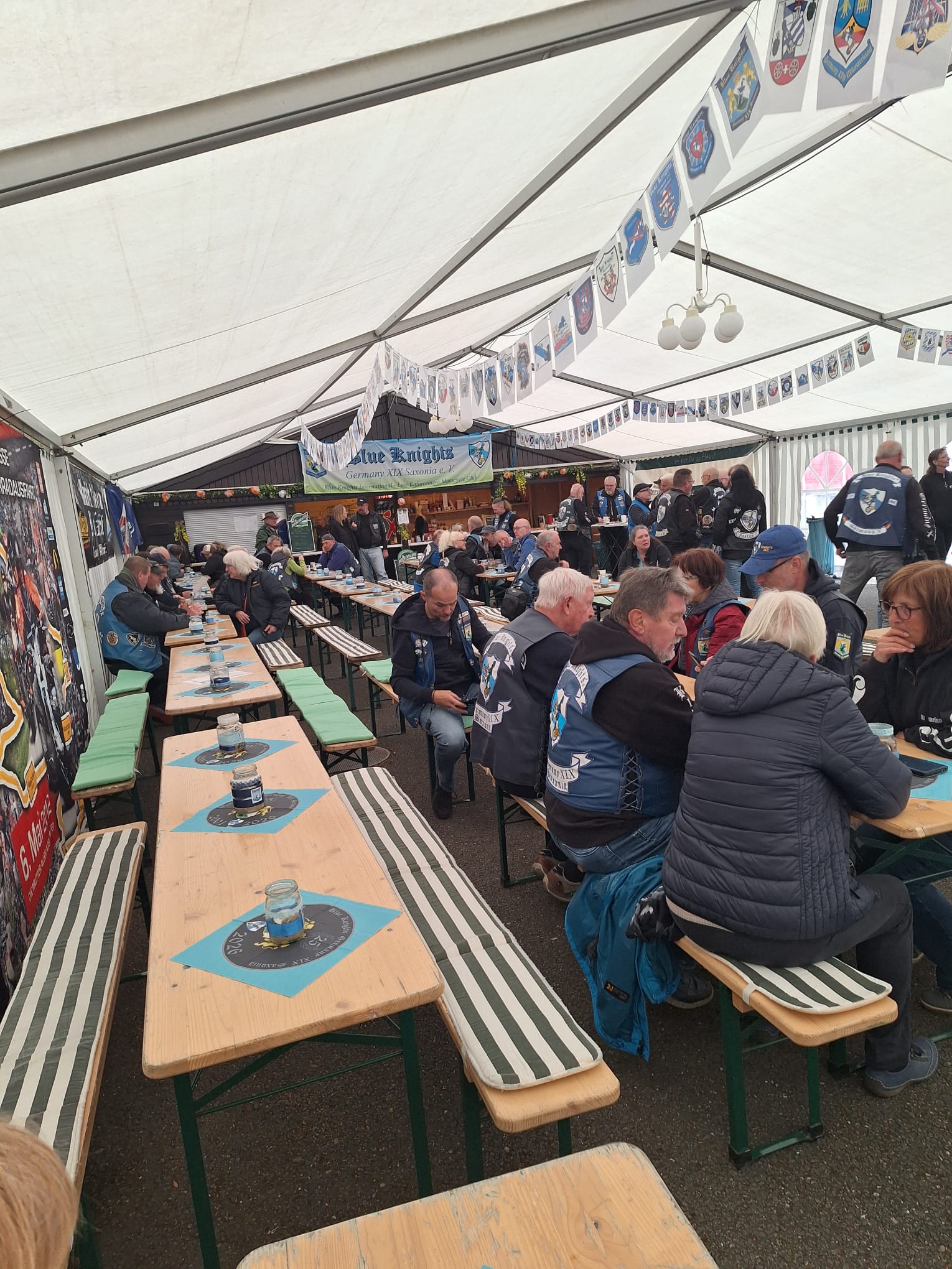 Innenraum des Festzelts mit langen Bierbänken, blauen Tischdecken und Wimpelketten
