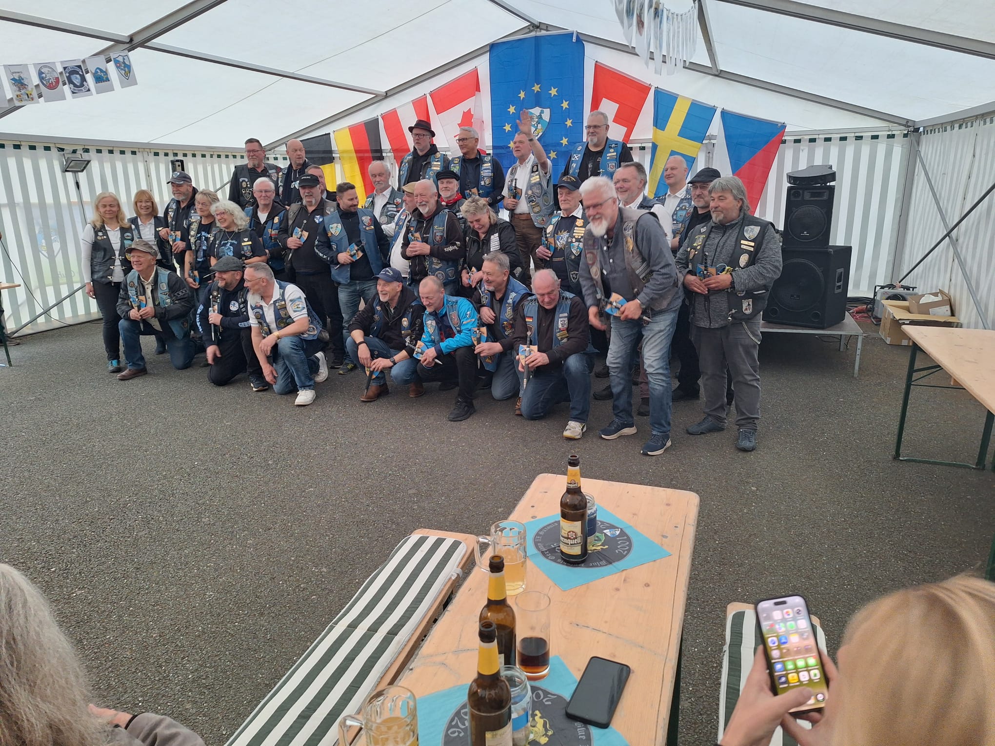 Großes Gruppenfoto im Festzelt vor den Nationalflaggen, rund dreißig Mitglieder