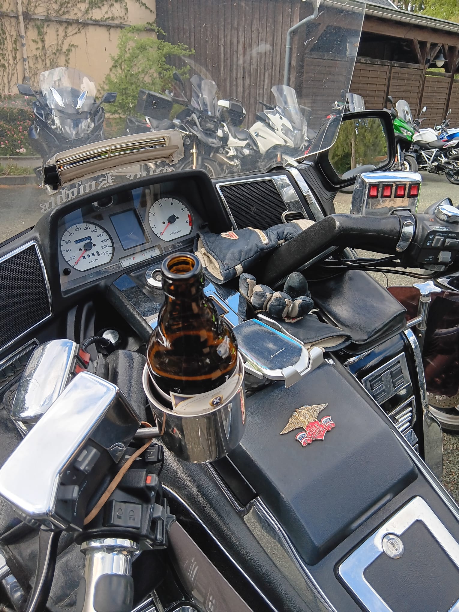 Eine braune Bierflasche steht im Becherhalter einer Honda Goldwing, im Hintergrund weitere Motorr&auml;der