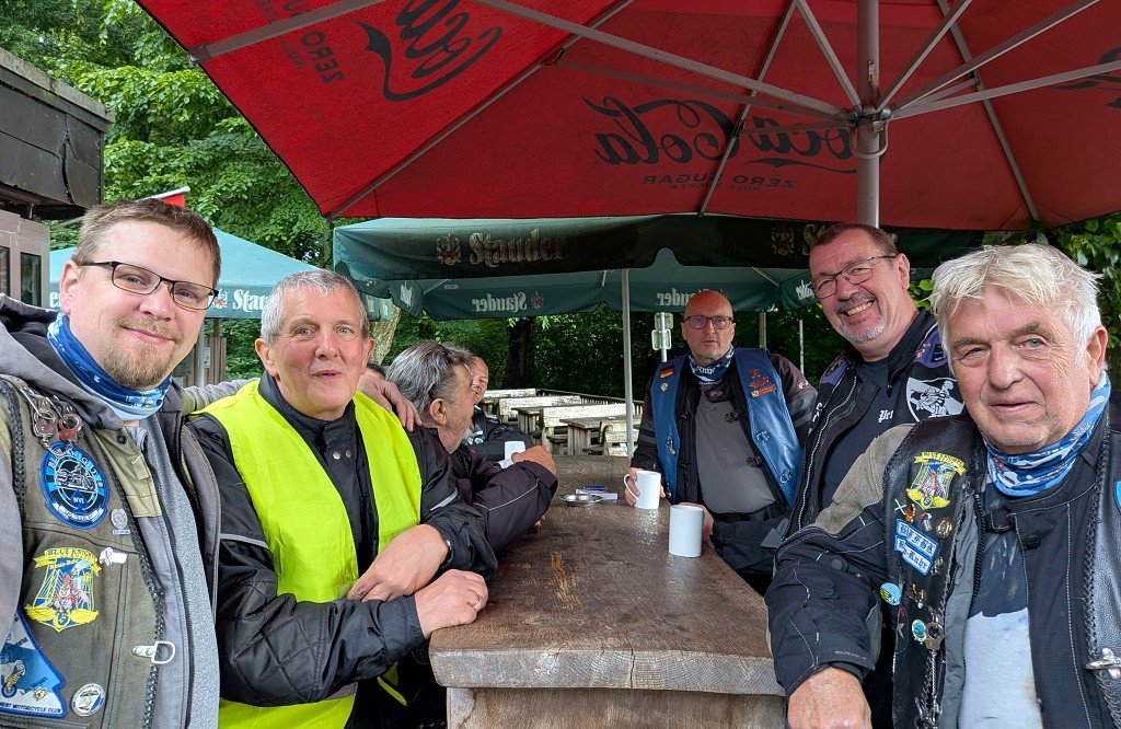 Gut gelaunte Mitglieder der Blue Knights Germany XVI an einem Biertisch unter rotem Sonnenschirm