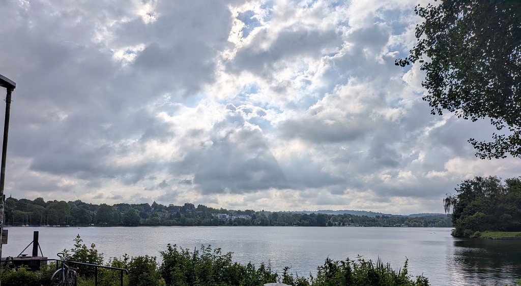 Stiller See im Morgengrauen mit dramatischem Wolkenhimmel und durchbrechenden Sonnenstrahlen vor dem Start